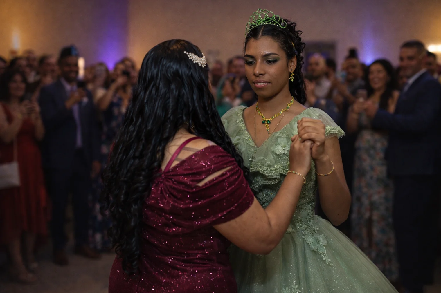 A quinceañera celebrant in a green gown dancing with a guest as others watch.