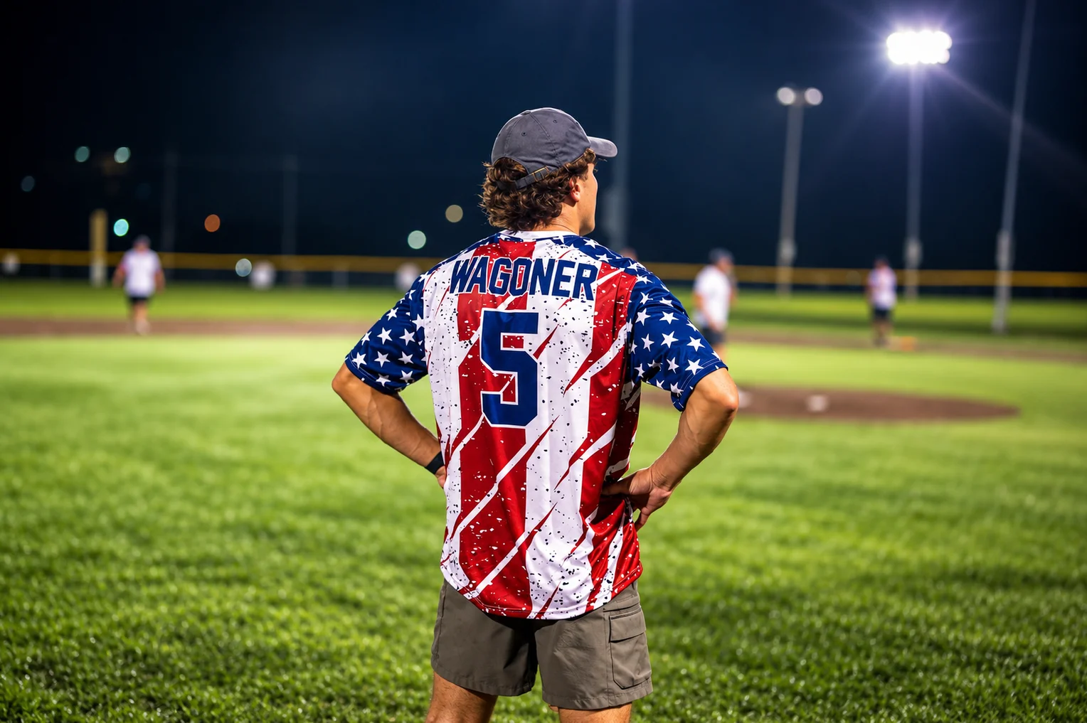 A softball player watching the field under stadium lights.
